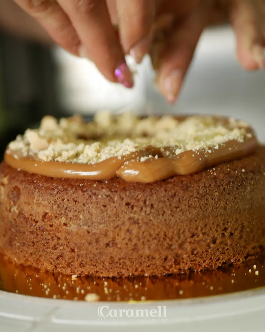 Manos terminando una torta de alfajor con arequipe y migas de galleta